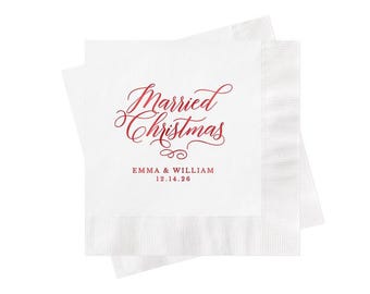 May include: Two stacked white paper napkins featuring red text that reads Married Christmas in a cursive script, followed by the names EMMA & WILLIAM and the date 12.14.26 in a simple serif font centered below the main script.