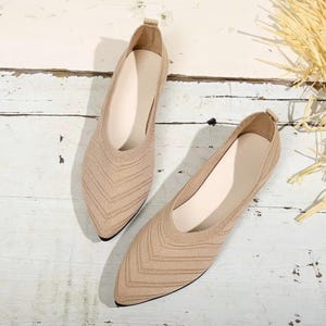 May include: A pair of beige knit flats with pointed toes. The shoes have a textured, chevron-like pattern on the upper and a neutral-colored insole. The flats are designed for comfort and style, suitable for everyday wear.