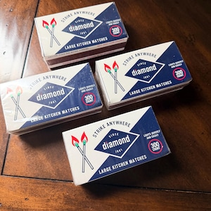 May include: Four rectangular boxes of Diamond brand large kitchen matches. Each white and blue box features the text Strike Anywhere, Diamond Since 1881, Large Kitchen Matches, and 300 Count, along with an illustration of two lit matches.