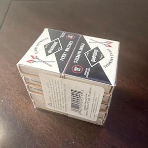 May include: A stack of Diamond Penny Matches boxes. The boxes are white with black and red accents, featuring the Diamond logo and the text "Strike Anywhere" and "Penny Matches". Each box contains 32 matches.