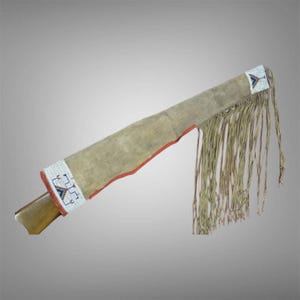 Può includere: Una custodia in pelle scamosciata color cuoio con lunghe frange, caratterizzata da una fascia di perline bianche sulla parte superiore e inferiore con motivi geometrici blu e rossi. La custodia ha un manico in legno marrone chiaro liscio.