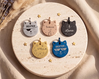 Peut inclure: Cinq médailles pour animaux en métal en forme de tête de chat avec des gravures. Les médailles sont argentées, or rose, noires, dorées et bleues. Elles portent des noms personnalisés comme Dexter, Simon, Luna et Stella avec divers motifs.