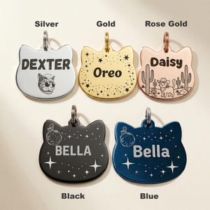 Peut inclure: Cinq m&eacute;dailles pour animaux en forme de t&ecirc;te de chat, disponibles en finitions argent, or, or rose, noir et bleu. Chaque m&eacute;daille poss&egrave;de un anneau m&eacute;tallique et des gravures personnalis&eacute;es : Dexter avec un chat, Oreo avec des &eacute;toiles, Daisy avec des cactus, et deux m&eacute;dailles Bella avec des motifs de lune et d'&eacute;toiles.