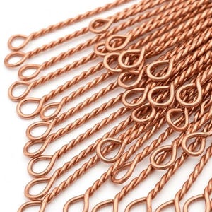 May include: A collection of copper-colored metal eye pins, each featuring a twisted wire shaft and a circular loop at one end. The pins are arranged in a parallel formation, showcasing the metallic texture and the uniform design of the wire components.