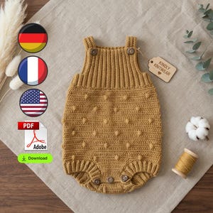 May include: A mustard yellow knitted romper featuring a textured bobble pattern, a ribbed bodice, and two buttons at the shoulder straps. The garment includes three buttons at the bottom leg openings and a tag labelled Kindly Knitwear.