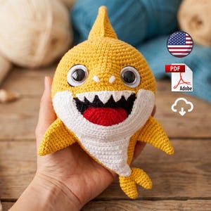 Peut inclure: Un jouet requin en crochet jaune avec un ventre blanc, une bouche noire avec des dents blanches, une langue rouge et deux grands yeux en plastique noir et blanc. Le requin possède une nageoire dorsale, deux nageoires latérales et une caudale.