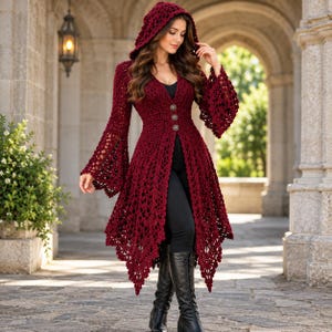 May include: A deep red, long-sleeved, hooded crochet cardigan featuring an open-knit pattern, flared bell sleeves, and three decorative metallic buttons down the front. The garment has an asymmetrical, pointed hemline that falls below the waist.