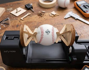 May include: A white baseball with red stitching held horizontally by two light-coloured wooden supports, mounted on a black eufy Make machine base. The baseball features a black logo with the text 08 in the centre.