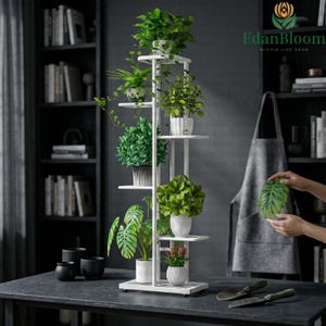 Puede incluir: Un estante para plantas blanco de varios niveles con varias plantas verdes en macetas. El estante tiene una base rectangular y varios estantes. Las plantas incluyen variedades frondosas, colgantes y florecientes. El estante está sobre una superficie oscura.