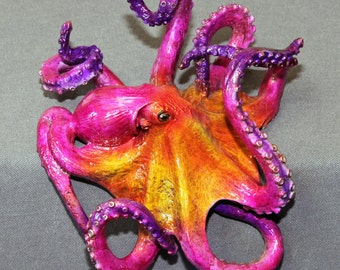 May include: A vibrant pink and yellow octopus sculpture with purple tentacles. The octopus is made of metal and has a detailed, realistic design.