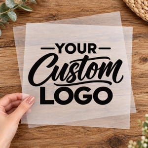 Peut inclure: Une feuille de pochoir carrée en plastique semi-transparent présentant le texte noir "YOUR" dans une police sans empattement grasse, suivi du mot "Custom" en écriture cursive fluide et "LOGO" en police sans empattement grasse.
