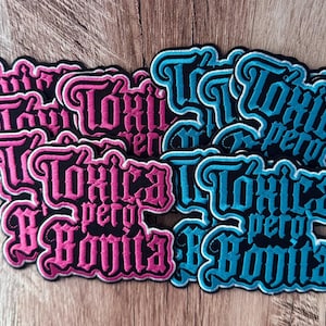 Könnte beinhalten: Eine Sammlung von gestickten Aufnähern mit dem Text Tóxica pero Bonita in einer Schriftart im gotischen Stil. Die Aufnäher sind in zwei Farbvarianten erhältlich: ein Set mit leuchtend rosa Garn auf schwarzem Grund und ein weiteres in leuchtendem Blau.