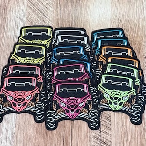 May include: A collection of embroidered patches shaped like off-road vehicles, each featuring a black base with a distinct neon-colored outline in yellow, blue, orange, pink, or green, and a leopard print pattern on the front bumper area.