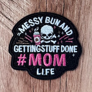 May include: A black embroidered patch featuring a white skull, a pink coffee cup, and the text "MESSY BUN AND GETTING STUFF DONE #MOM LIFE" in white and pink thread. The patch has a rounded shape with a black border and decorative star accents.