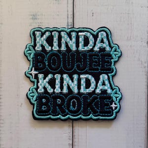 May include: A rectangular embroidered patch with a black background and a teal border. The text reads KINDA BOUJEE KINDA BROKE in alternating rows of white and teal chequered lettering and solid black lettering, accented by small white star symbols.