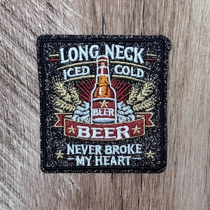 Puede incluir: Un parche rectangular bordado con purpurina negra que presenta un gráfico central de una botella de cerveza ámbar. El texto dice LONG NECK, ICED COLD, BEER y NEVER BROKE MY HEART. El diseño incluye espigas de trigo doradas y conos de lúpulo.