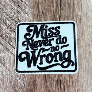 May include: A square embroidered patch with a white background and a black border. The patch features the black embroidered text "Miss Never do no Wrong" in a stylised, cursive-inspired font, centred within the square frame.