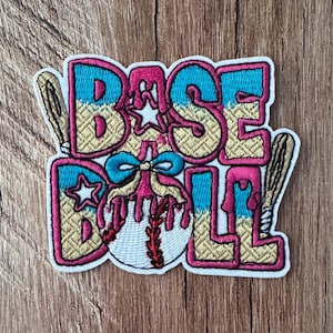 May include: An embroidered patch featuring the word BASEBALL in bold pink-outlined letters with a blue and tan textured fill. A white baseball with red stitching, a blue bow, and two tan baseball bats are integrated into the design.