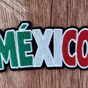 May include: An embroidered patch featuring the word MÉXICO in bold, block letters. The letters M and E are green, the X and I are white, and the C and O are red. Each letter is outlined in white thread, and the entire word has a black border.