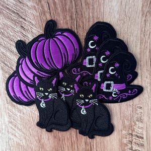 May include: A collection of embroidered patches featuring purple pumpkins, black cats with purple collars and silver moon charms, and black witch hats decorated with purple bands, silver buckles, and white crescent moon and star embroidery details.