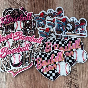 Puede incluir: Una colección de parches bordados con temática de béisbol. Algunos muestran el texto Baseball Mom en letra rosa sobre fondos de estampado de leopardo o corazones a cuadros, mientras que otros incluyen pelotas, bates y guantes en rojo y azul.