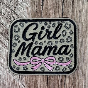Könnte beinhalten: Ein rechteckiger bestickter Aufnäher mit abgerundeten Ecken, der einen hellolivgrünen Hintergrund mit einem dunkelgrauen Leopardenmuster aufweist. Der Text Girl Mama ist in schwarzer Schreibschrift gestickt, mit einer rosa Schleife darunter.