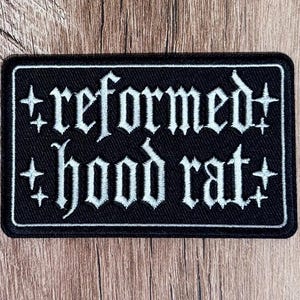 Op de afbeelding: Een rechthoekige zwarte geborduurde patch met een witte rand. De tekst 'reformed hood rat' is in een wit gotisch lettertype in het midden geborduurd en wordt aan weerszijden geflankeerd door vier kleine witte vierpuntige sterren.