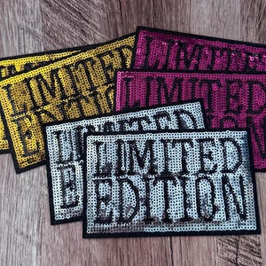 May include: A collection of rectangular patches featuring the text LIMITED EDITION in black block letters. The patches are covered in shimmering sequins and come in gold, magenta, and silver colors, each outlined with a solid black border.