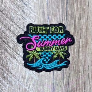 Op de afbeelding: Een zwarte geborduurde patch met de tekst BUILT FOR Summer SUNNY DAYS in limoengroen en roze. Het ontwerp bevat een blauwgroene en zwarte geblokte driehoek, twee limoengroene palmbomen en gestileerde blauwgroene oceaangolven onderaan.