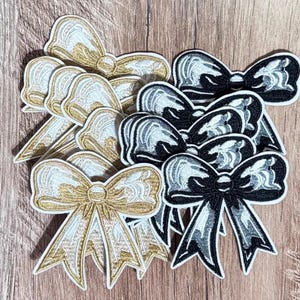May include: A collection of embroidered bow patches in metallic gold and black thread. Each bow features a detailed stitched texture with a central knot and two hanging ribbon tails. The patches are arranged in a layered cluster.