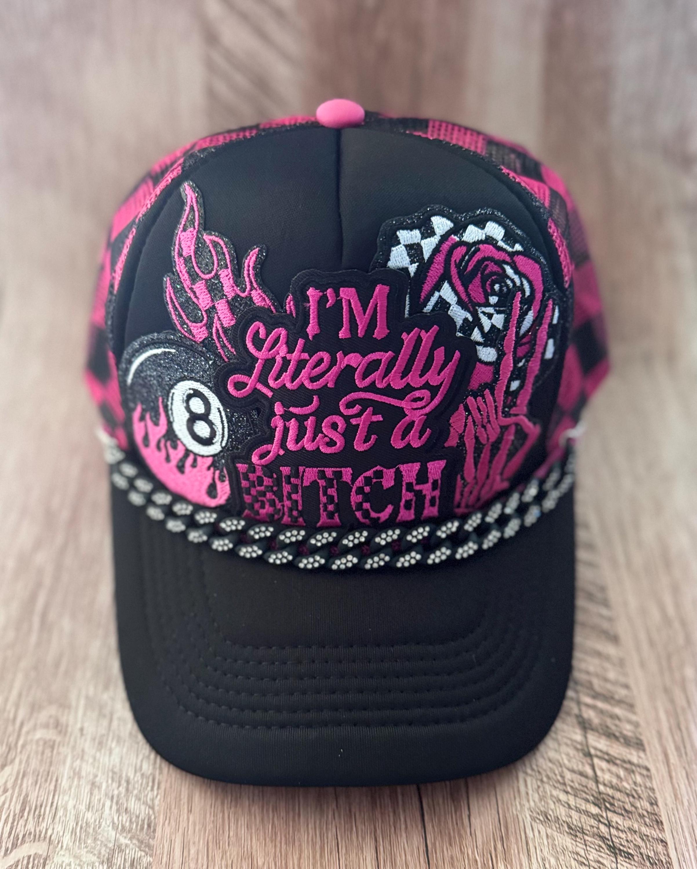 May include: A black trucker hat featuring a pink and black checkered pattern on the sides and back. The front panel displays a glittery graphic with an eight ball, a rose, and the text I'M Literally just a BITCH. A silver chain trim accents the brim.