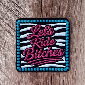 May include: A square embroidered patch featuring a black and white zebra stripe pattern background. The text Let's Ride Bitches is stitched in bright pink cursive lettering. The border consists of a continuous row of small, circular turquoise blue stitches.