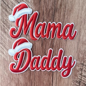 以下が含まれることがあります： 赤の筆記体でMamaとDaddyと書かれた刺繍ワッペン2枚。それぞれの単語の上に赤と白のサンタクロースの帽子があしらわれています。ワッペンには白い縁取りがあり、衣類やアクセサリーに取り付けられるようにデザインされています。
