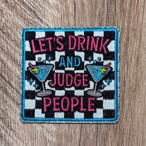 May include: A square embroidered patch with a black and white checkered background and a shimmering blue border. It features two blue martini glasses with olives and the pink and blue text: LET'S DRINK AND JUDGE PEOPLE, arranged in three lines.