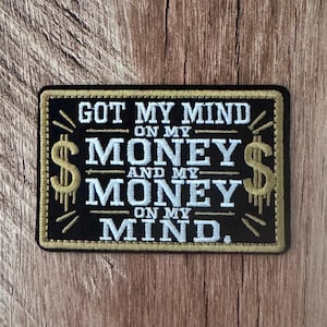 May include: A rectangular embroidered patch with a black background and a gold border. The text reads GOT MY MIND ON MY MONEY AND MY MONEY ON MY MIND in white lettering. Two gold dollar signs are embroidered on the left and right sides of the text.