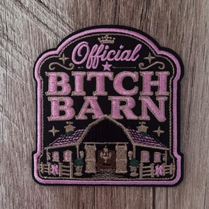 May include: A black embroidered patch with a pink border featuring the text Official BITCH BARN in pink lettering. Below the text is an illustration of a barn with a chandelier inside, accented with pink details, stars, and a small crown icon.