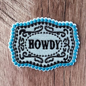 Pode incluir: Um emblema bordado retangular com fundo azul claro e borda festonada com costura em azul brilhante. O centro exibe a palavra HOWDY em letras pretas em negrito, cercada por arabescos pretos intrincados e uma borda pontilhada.