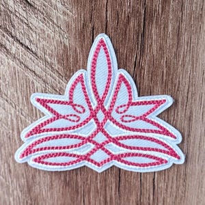 May include: A white embroidered patch featuring a symmetrical, stylized floral or leaf-like design outlined in vibrant pink thread. The intricate pattern consists of interconnected, curved lines that form a pointed, multi-layered shape.