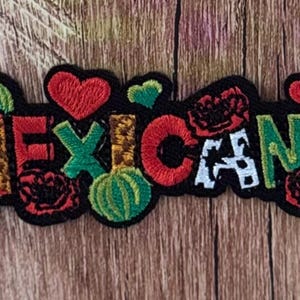 Puede incluir: Un parche bordado con la palabra MEXICANA en letras coloridas y estampadas. El diseño incluye corazones rojos, cactus verdes y flores rojas, todo delineado con hilo negro, creando un accesorio textil decorativo y muy detallado.
