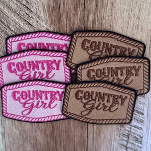 May include: A collection of rectangular embroidered patches featuring a rope-style border. Three patches are light pink with dark pink text reading Country Girl, and three patches are tan with dark brown text reading Country Girl.