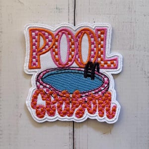 May include: An embroidered patch featuring the text POOL SEASON in orange and pink checkered lettering. Between the words is a depiction of a blue swimming pool with a black ladder, all outlined in white thread against a white background.