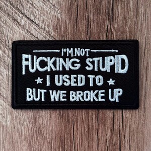 May include: A rectangular black embroidered patch featuring white stitched text that reads I'M NOT FUCKING STUPID I USED TO BUT WE BROKE UP, with two small stars flanking the middle line of text and horizontal lines above and below the top phrase.