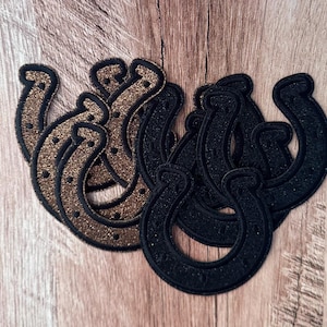 May include: A collection of horseshoe-shaped patches featuring a glittery texture. The set includes several patches in a metallic gold finish and several patches in a solid black finish, each with a stitched border and small dot details.