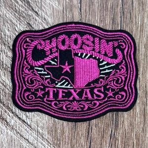 May include: A rectangular embroidered patch with a black background and vibrant pink stitching. The design features the text CHOOSIN and TEXAS, a silhouette of the state of Texas with a star, and decorative scrollwork borders throughout.