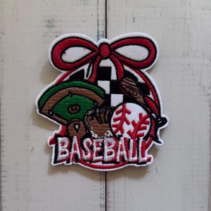 May include: An embroidered patch featuring a red bow at the top, a green baseball field, a brown glove, a white baseball with red stitching, and a black and white checkered pattern. The word BASEBALL is stitched in white with a red outline.