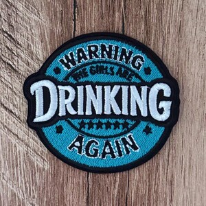 May include: A circular embroidered patch with a bright blue background and a black border. The text reads WARNING THE GIRLS ARE DRINKING AGAIN in white and black lettering. Five small black stars are centred between the words DRINKING and AGAIN.