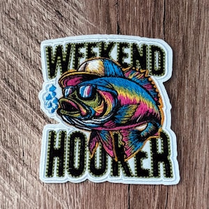 May include: An embroidered patch featuring a colorful fish wearing a yellow cap and sunglasses, with blue bubbles to the left. The text WEEKEND HOOKER is stitched in black with a light green border above and below the fish illustration.