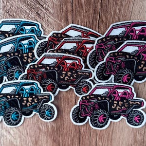 May include: A collection of embroidered patches featuring off-road vehicle designs. Each patch displays a side-profile of a utility terrain vehicle with a leopard print body pattern, available in either bright blue or vibrant pink accent colors.