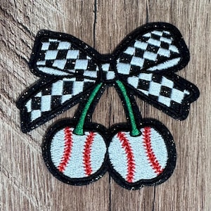 May include: An embroidered patch featuring two baseballs designed to look like cherries, with red stitching and green stems, topped with a black and white checkered bow. The entire design is outlined in a black border with a subtle glittery finish.
