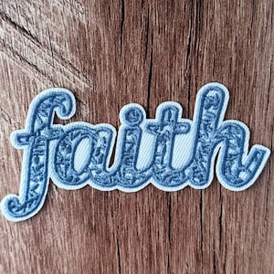 May include: An embroidered patch featuring the word faith in a cursive script font. The lettering is filled with a dark blue floral pattern and outlined in a thick, light blue border, creating a distinct contrast against the background.